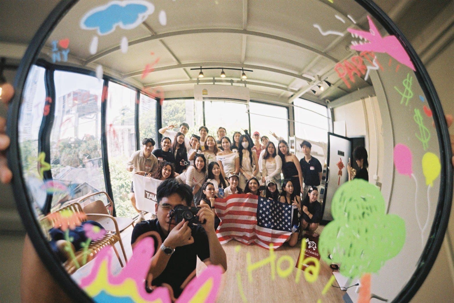 ภาพมุมกว้างผ่านกระจกกลม ผู้ร่วมงานถือธงอเมริกาในงาน Dek Work Party